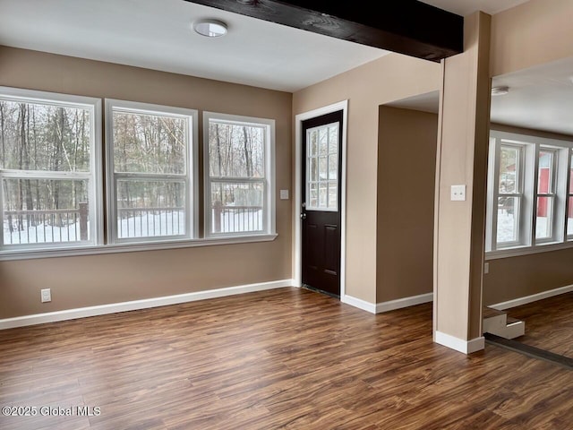 foyer entrance featuring dark wood-style floors, beamed ceiling, a wealth of natural light, and baseboards