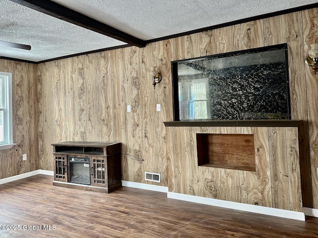 unfurnished living room featuring a textured ceiling, wood finished floors, visible vents, baseboards, and beamed ceiling