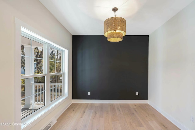 unfurnished room with an accent wall, light wood-style flooring, baseboards, and an inviting chandelier