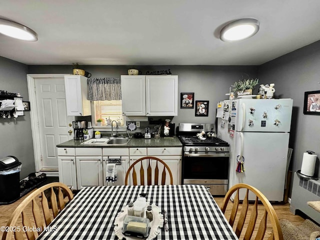 kitchen featuring stainless steel range with gas cooktop, dark countertops, freestanding refrigerator, white cabinetry, and a sink