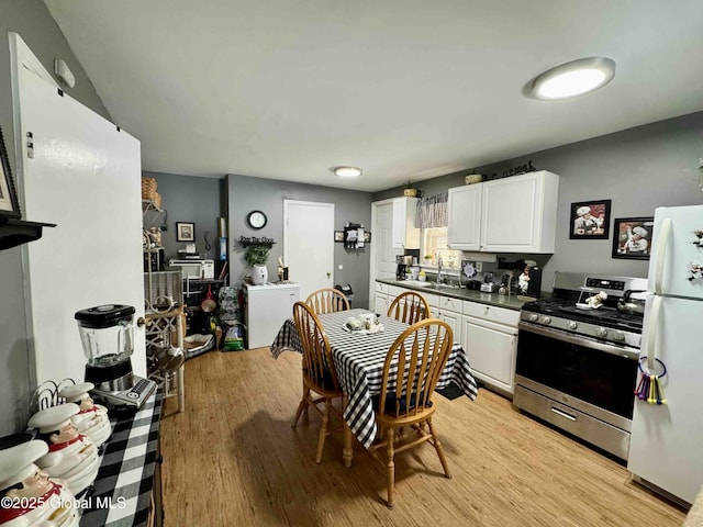 kitchen with stainless steel gas range oven, white cabinets, dark countertops, freestanding refrigerator, and a sink