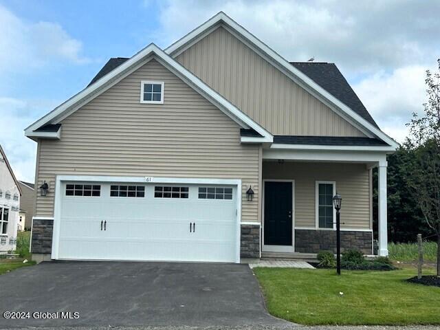 craftsman inspired home with a garage, stone siding, driveway, and a front lawn