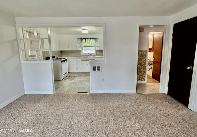 kitchen with gas range gas stove, a sink, light countertops, white cabinetry, and light colored carpet