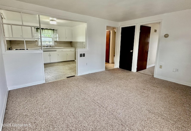 kitchen featuring white cabinetry, light colored carpet, baseboards, and backsplash