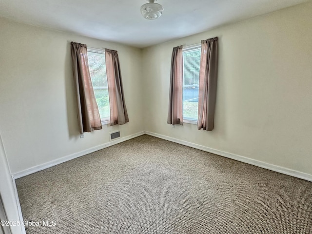 empty room featuring a wealth of natural light, carpet flooring, visible vents, and baseboards