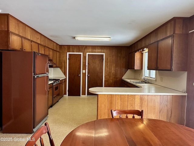 kitchen with light countertops, a peninsula, freestanding refrigerator, gas stove, and a sink