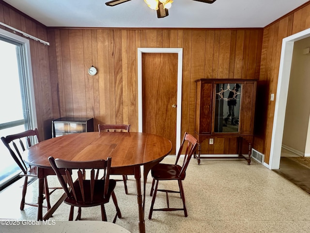 dining area featuring a ceiling fan, visible vents, wood walls, and baseboards