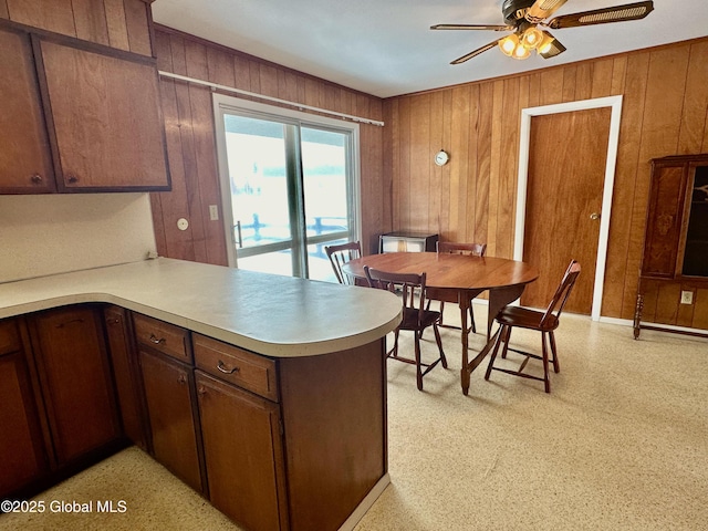 kitchen featuring light floors, a peninsula, ceiling fan, light countertops, and wood walls