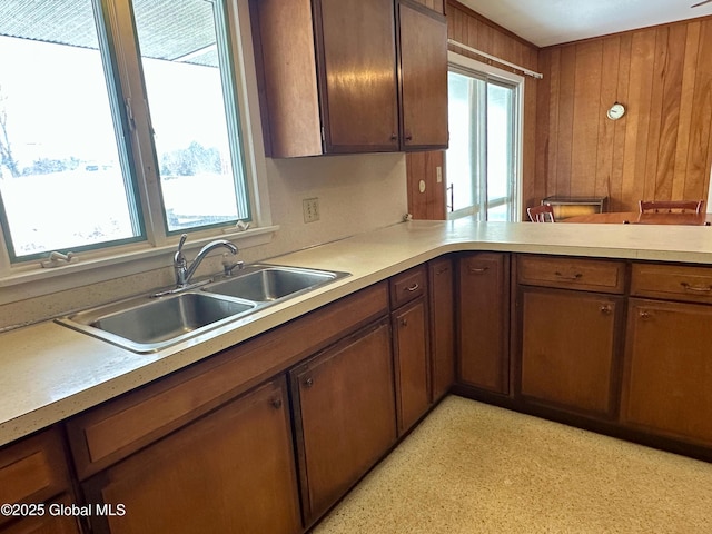 kitchen featuring light countertops, a peninsula, wood walls, and a sink