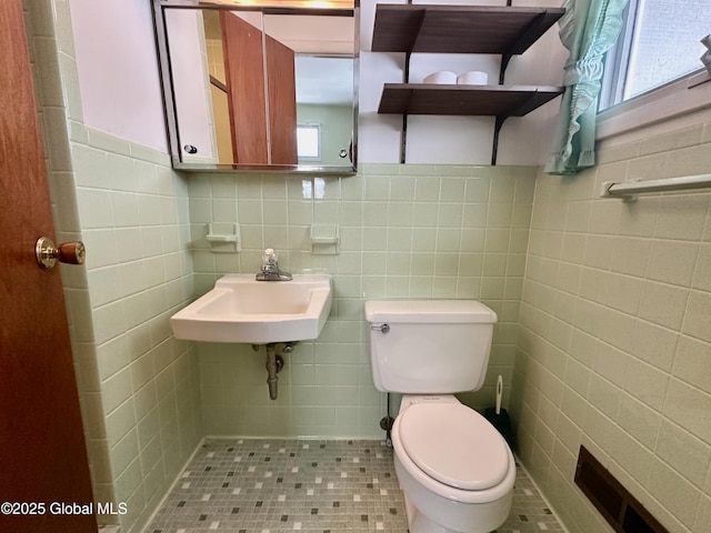 bathroom with visible vents, toilet, tile walls, and a sink