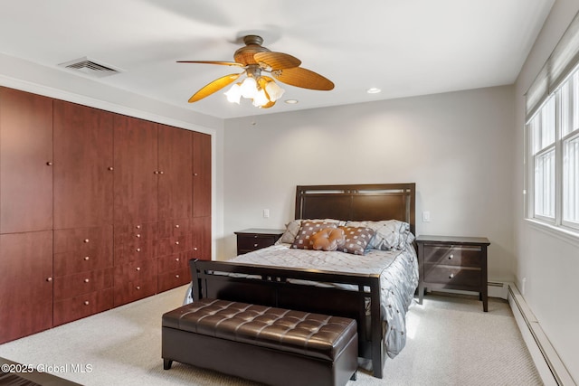 bedroom with a baseboard heating unit, a closet, light carpet, and visible vents