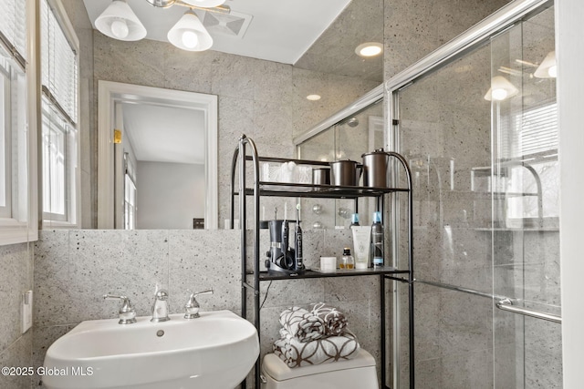 bathroom with toilet, a shower stall, tile walls, and a sink