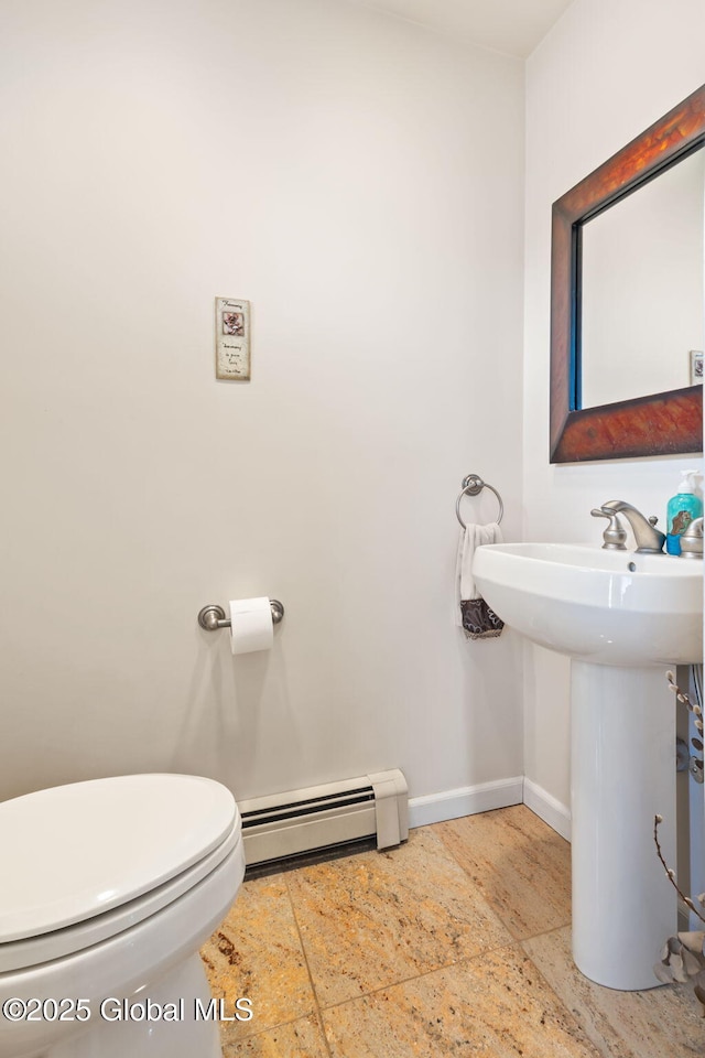 bathroom with stone tile flooring, toilet, baseboard heating, a sink, and baseboards