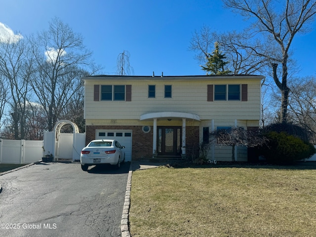 colonial home with aphalt driveway, a gate, fence, a front lawn, and brick siding