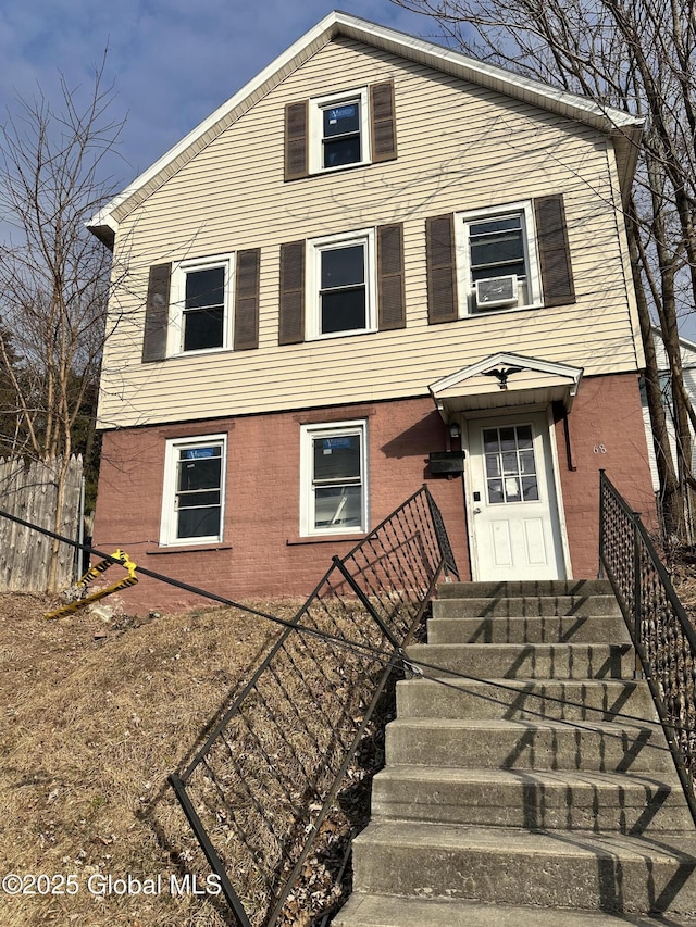 view of front facade featuring brick siding, cooling unit, and fence