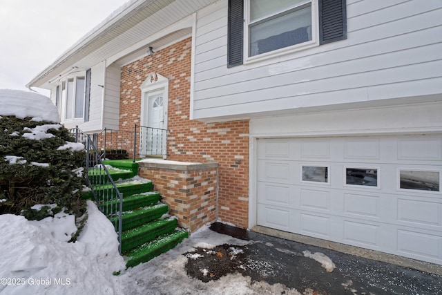 snow covered property entrance featuring a garage and brick siding