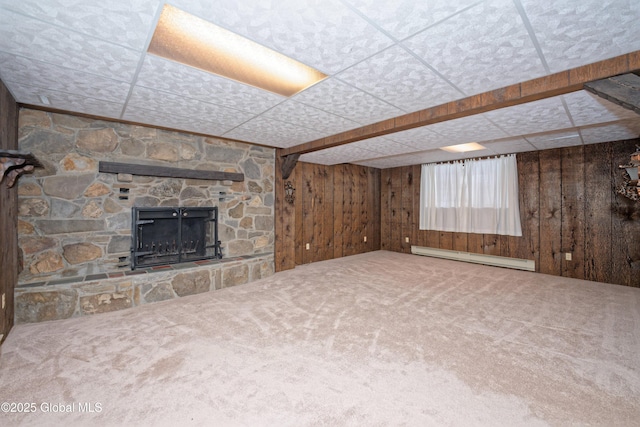 unfurnished living room featuring a fireplace, baseboard heating, carpet flooring, wood walls, and a drop ceiling