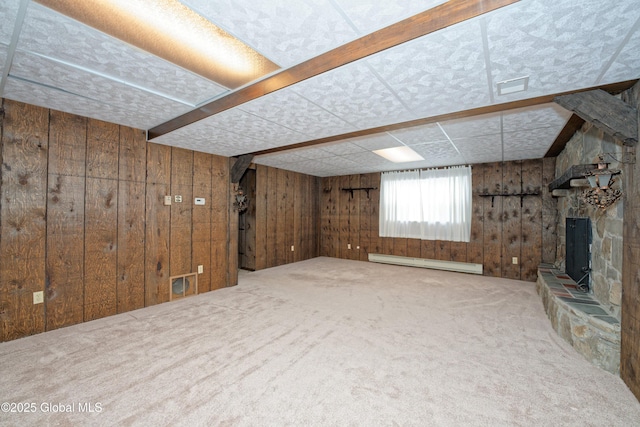 basement with carpet floors, visible vents, baseboard heating, wood walls, and a stone fireplace