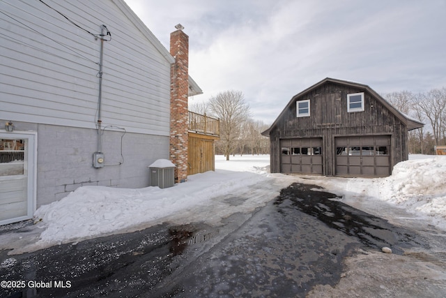 view of snow covered exterior featuring a detached garage, an outdoor structure, and a gambrel roof