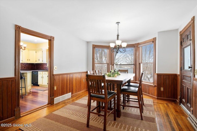 dining room featuring hardwood / wood-style floors, wainscoting, visible vents, and an inviting chandelier