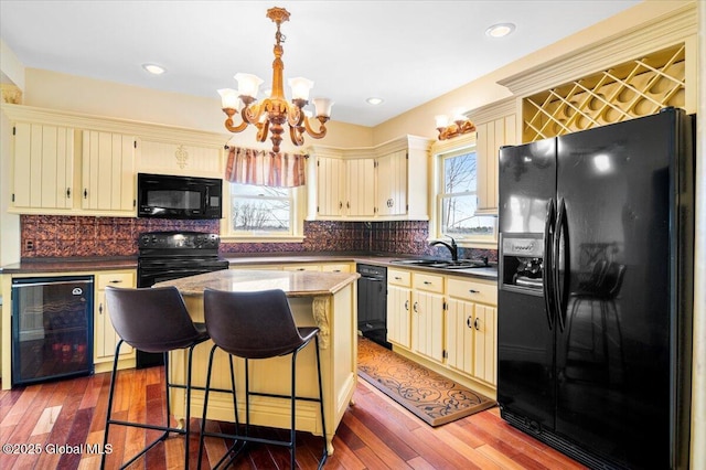 kitchen with wine cooler, a sink, a center island, black appliances, and decorative light fixtures