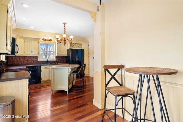 kitchen featuring a kitchen island, hanging light fixtures, black appliances, dark countertops, and a kitchen bar