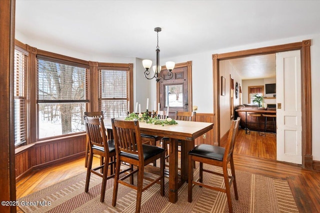 dining space featuring a chandelier, wainscoting, wood finished floors, and wooden walls