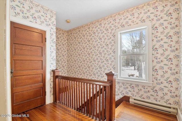 interior space with wallpapered walls, a baseboard radiator, and wood finished floors