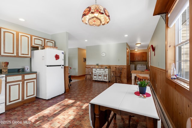 kitchen with brick floor, washing machine and clothes dryer, wainscoting, wooden walls, and white appliances