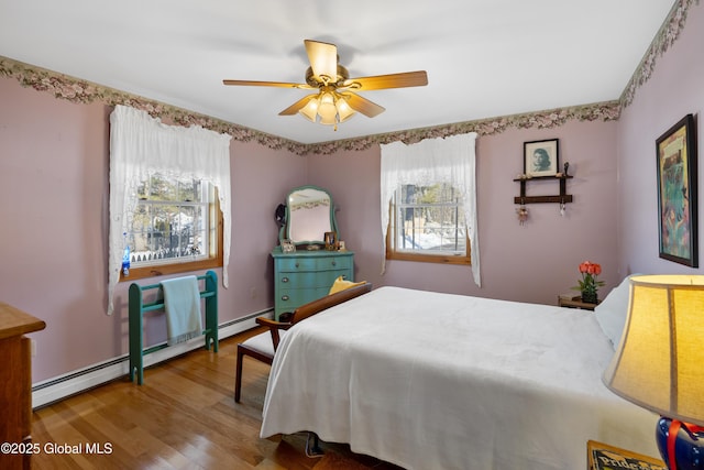 bedroom featuring ceiling fan, a baseboard heating unit, and wood finished floors