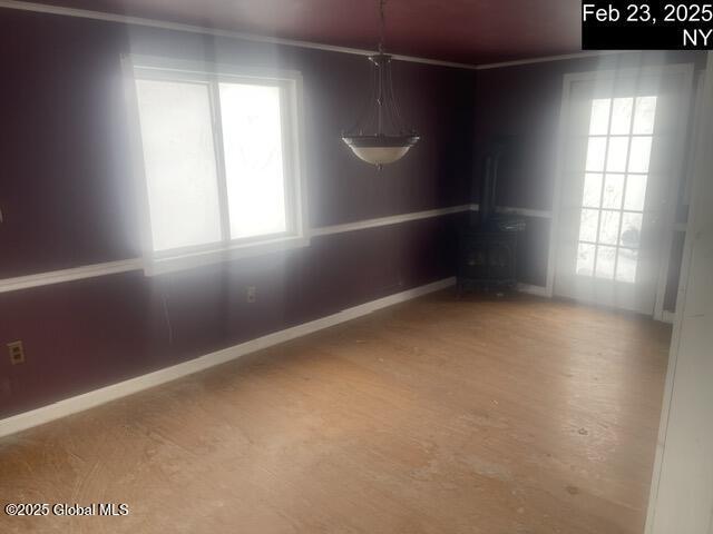 unfurnished dining area featuring a wood stove, a healthy amount of sunlight, crown molding, and baseboards