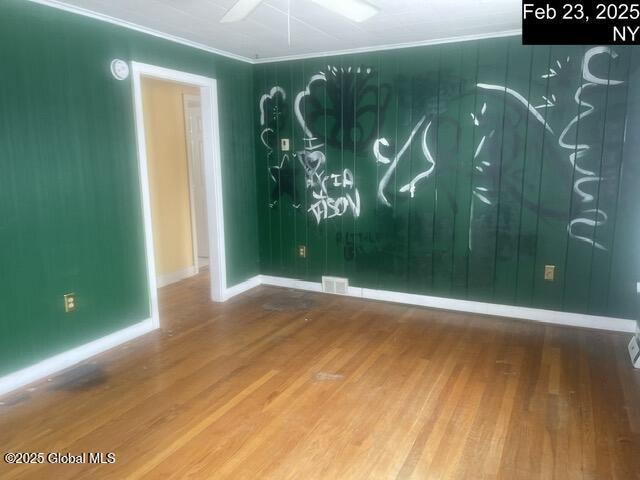 spare room featuring baseboards, visible vents, crown molding, and wood finished floors