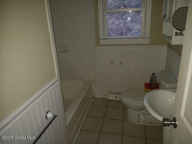 bathroom featuring a bathing tub, toilet, a sink, wainscoting, and tile patterned floors