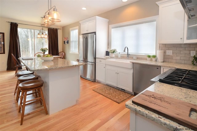 kitchen with a kitchen island, appliances with stainless steel finishes, decorative light fixtures, white cabinetry, and a sink