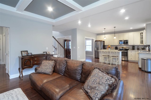 living area featuring baseboards, dark wood finished floors, beamed ceiling, and stairs