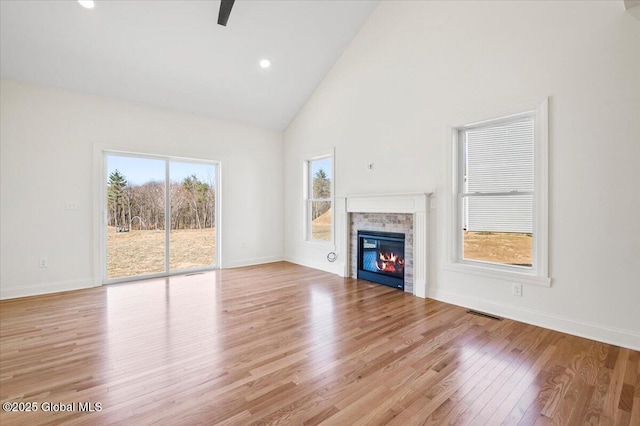 unfurnished living room with baseboards, high vaulted ceiling, wood finished floors, and a tile fireplace