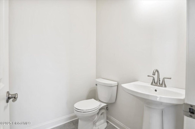 half bathroom with toilet, a sink, and baseboards