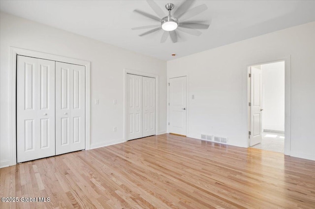 unfurnished bedroom with visible vents, two closets, baseboards, light wood-type flooring, and ensuite bath