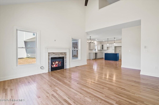 unfurnished living room with an inviting chandelier, baseboards, a towering ceiling, light wood-style flooring, and a glass covered fireplace