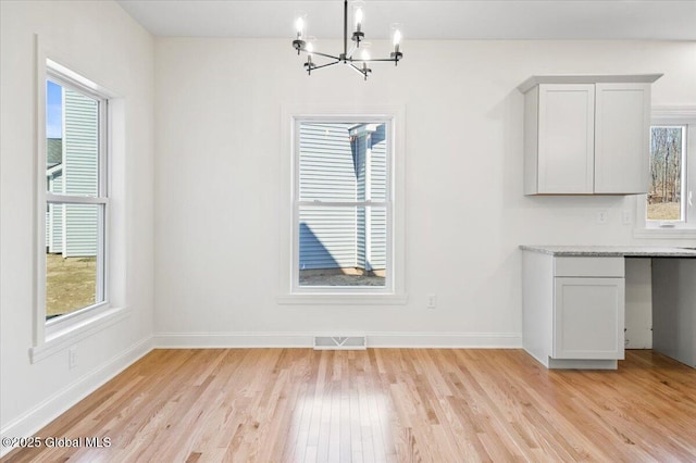 unfurnished dining area featuring baseboards, visible vents, light wood-style floors, and a notable chandelier