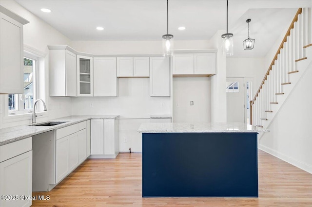 kitchen featuring light wood finished floors, white cabinetry, light stone counters, and a sink