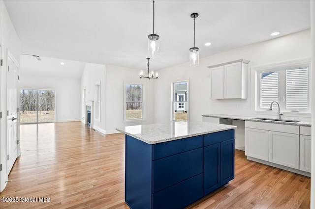kitchen featuring a chandelier, a kitchen island, a sink, light wood-style floors, and pendant lighting
