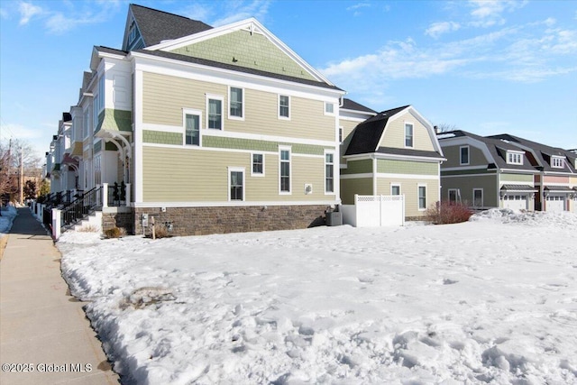 snow covered rear of property featuring a residential view, a garage, and a gambrel roof