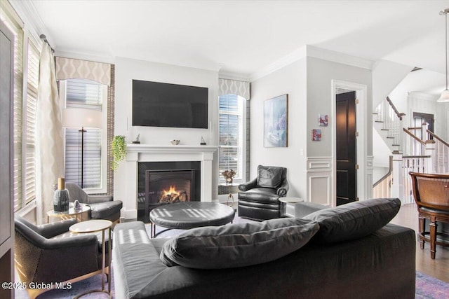 living area with a warm lit fireplace, wood finished floors, stairs, and crown molding