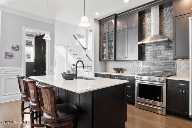 kitchen with a sink, backsplash, wall chimney range hood, stainless steel gas stove, and dark wood-style flooring