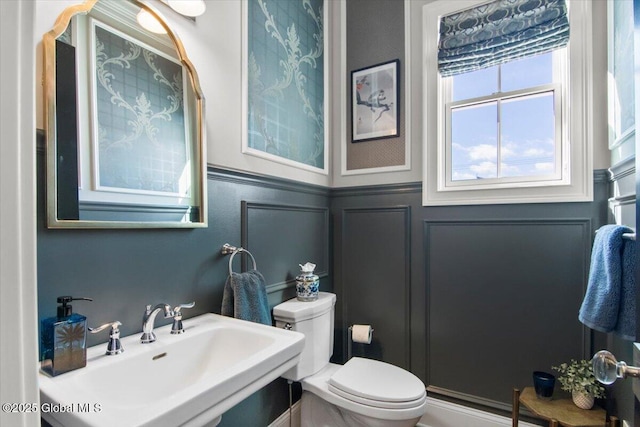 bathroom with a sink, a wainscoted wall, toilet, and a decorative wall