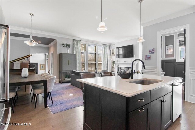 kitchen with wood finished floors, a sink, light countertops, stainless steel dishwasher, and open floor plan