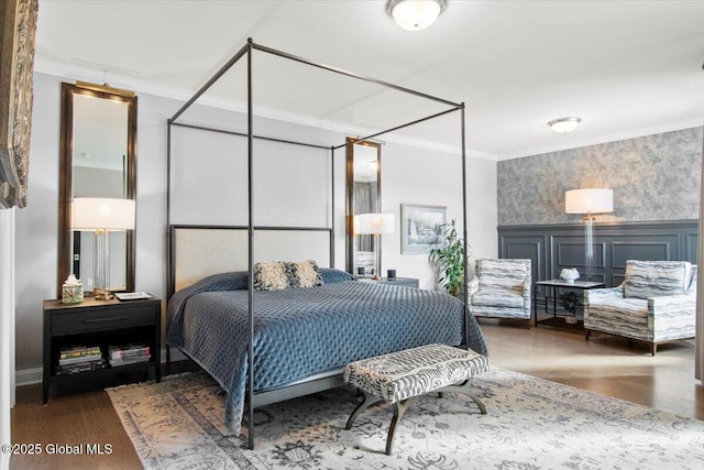 bedroom with a wainscoted wall, ornamental molding, wallpapered walls, wood finished floors, and a decorative wall