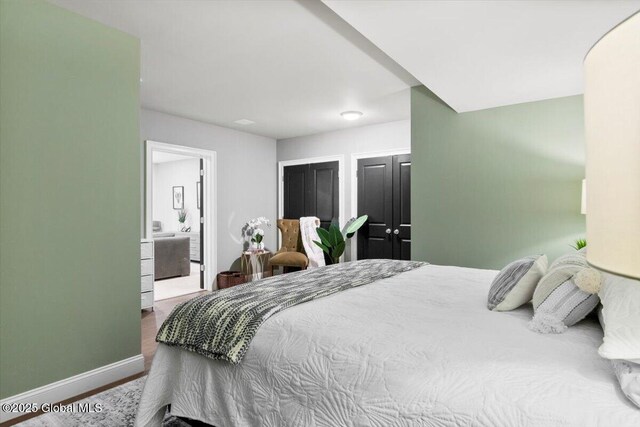 bedroom with wood finished floors, baseboards, and multiple closets