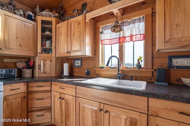 kitchen with glass insert cabinets, dark countertops, a sink, and wooden walls